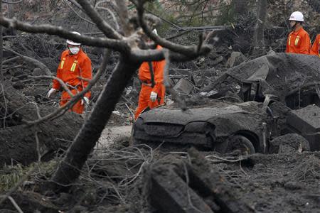 Rescuers walk past a wrecked car on a damaged road covered with debris a day after an explosion at a Sinopec Corp oil pipeline in Huangdao, Qingdao, Shandong Province November 23, 2013. REUTERS/Aly Song