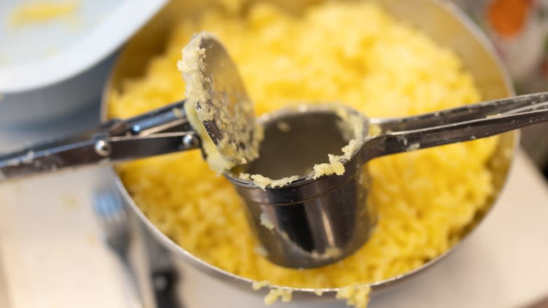 A potato ricer over a pot of riced potatoes