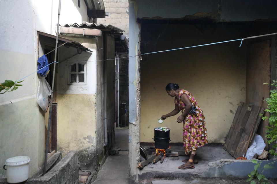 FILE - A woman cooks using a firewood hearth outside her house amid shortage of cooking gas in Colombo, Sri Lanka, on June 23, 2022. As food costs and fuel bills soar, inflation is plundering people’s wallets, sparking a wave of protests and workers’ strikes around the world. (AP Photo/Eranga Jayawardena)