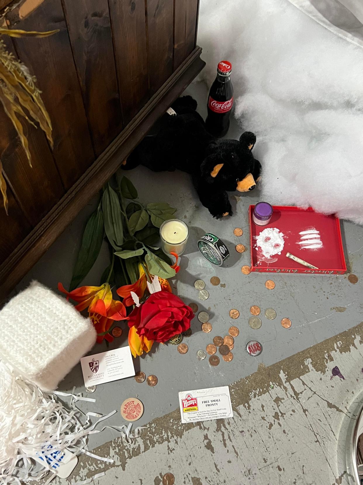 Trinkets — including a stuffed bear, knitted cocaine and fake lines of the drug — line the floor at the base of a taxidermed bear in Kentucky. There's also change, flowers, and a candle. (Courtesy of Courtney Oldendorf)