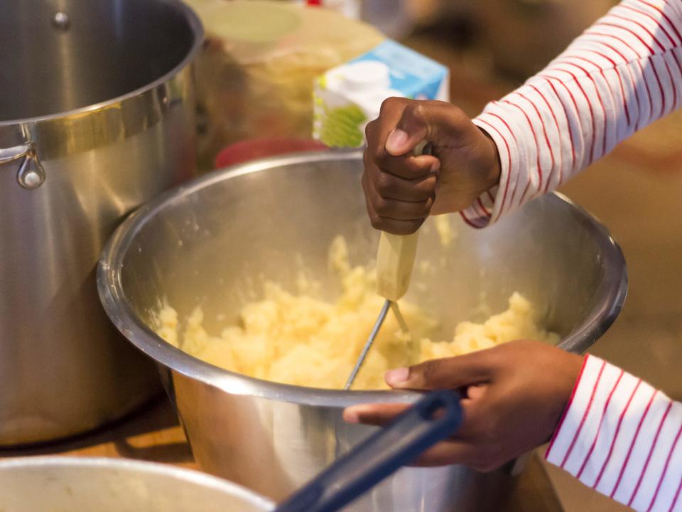 a person hand mashing potatoes in a silver bowl