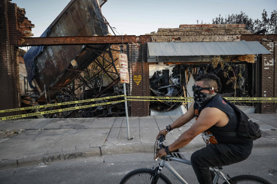 FILE - In this June 1, 2020, file photo, a cyclist passes burned-out businesses along East Lake Street that were destroyed in protests two nights earlier in Minneapolis. An external review of Minnesota's response to the civil unrest following the May 2020 killing of George Floyd found several weaknesses, including a lack of clear leadership early on as businesses were being destroyed and set ablaze, and a failure to discern peaceful from unlawful protesters. (AP Photo/John Minchillo, file)