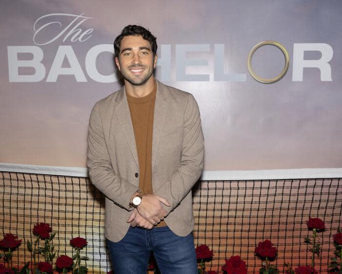 'The Bachelor' star Joey Graziadei smiles in front of a Bachelor TV show poster