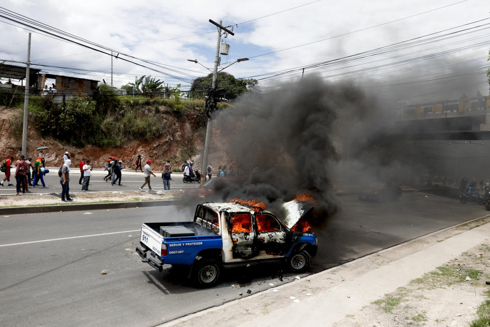 Demonstrators walk past a torched police vehicle during a protest against the government of Honduras' President Juan Orlando Hernandez in Tegucigalpa, Honduras, Thursday, May 30, 2019. Thousands of doctors and teachers have been marching through the streets of Honduras' capital for the last three weeks, against presidential decrees they say would lead to massive public sector layoffs. (AP Photo/Elmer Martinez)