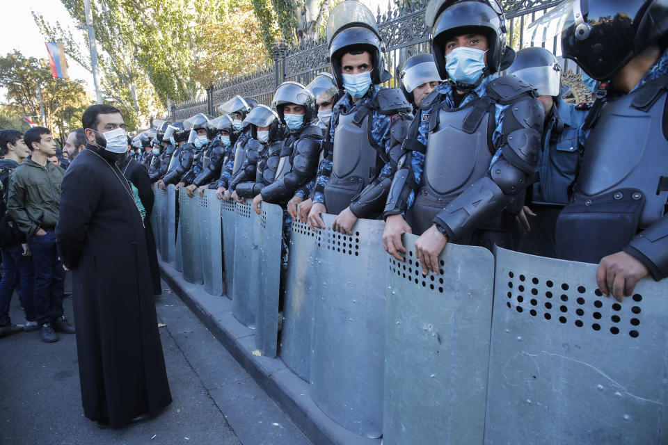 An Orthodox priest stands next to police guard during a protest against an agreement to halt fighting over the Nagorno-Karabakh region, in Yerevan, Armenia, Wednesday, Nov. 11, 2020. Thousands of people flooded the streets of Yerevan once again on Wednesday, protesting an agreement between Armenia and Azerbaijan to halt the fighting over Nagorno-Karabakh, which calls for deployment of nearly 2,000 Russian peacekeepers and territorial concessions. Protesters clashed with police, and scores have been detained. (AP Photo/Dmitri Lovetsky)