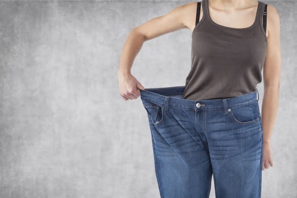 A person holding out the waist of their jeans to show that the jeans are too big for them.