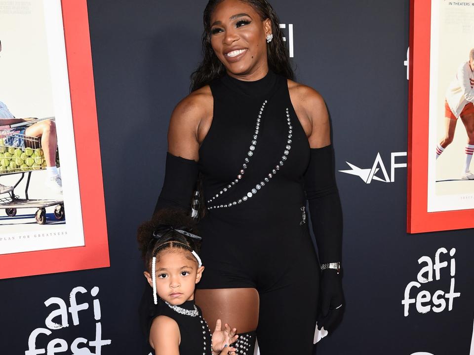 Olympia Ohanian and Serena Williams, both wearing black dresses, pose against a black background.