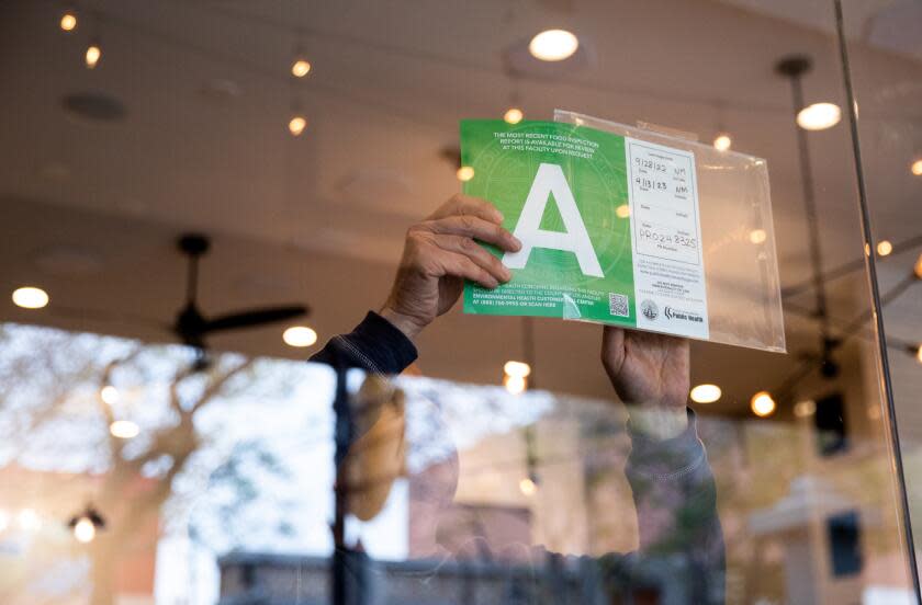 Wild Carvery owner Vahe Aiwazian puts his newly updated A health inspection score in the window after Ngoc McShane, environmental health specialist, completed her inspection at the restaurant in Burbank on April 13, 2023. (Alisha Jucevic/For The Times)