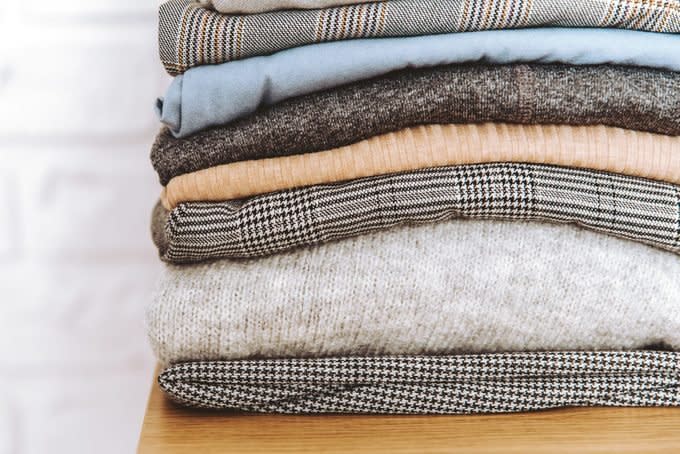 Stack of neatly folded clothes of wool, cotton, linen, silk, polyester on wood surface with white wall background