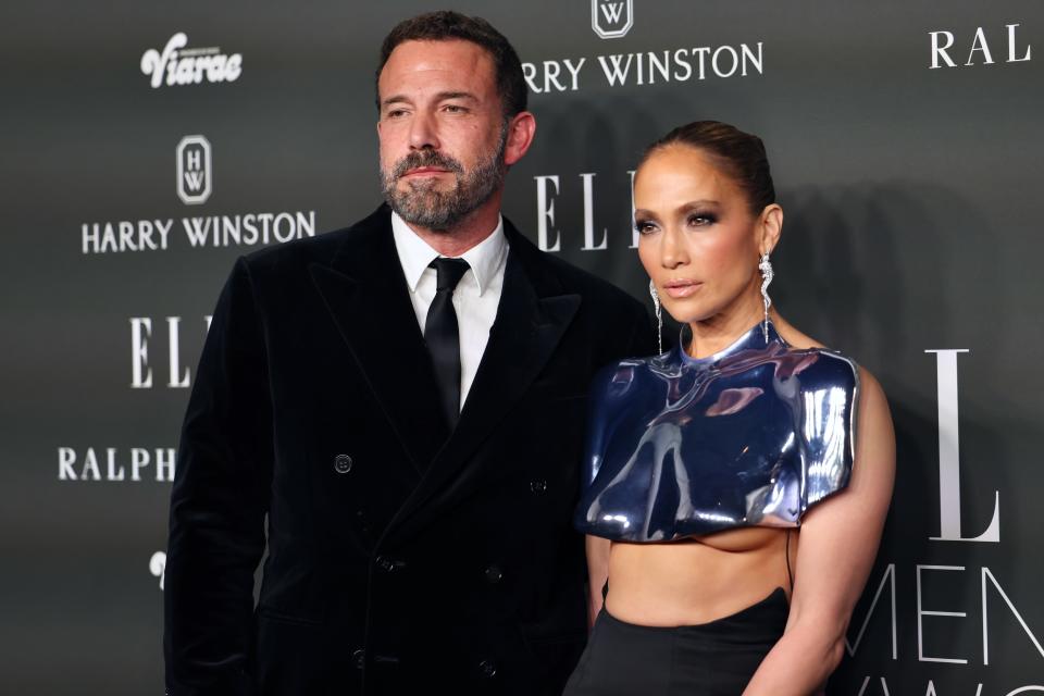 Ben Affleck in a black suit and tie, and Jennifer Lopez in a futuristic cropped top and skirt, pose together at an event