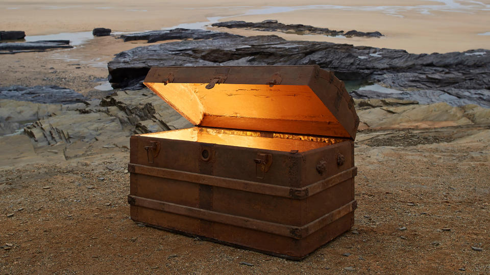 Open treasure chest of gold on a deserted beach.