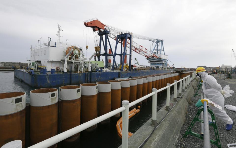 A Tokyo Electric Power Co. (TEPCO) employee wearing a protective suit and mask stands next to an impervious wall made of a steel pipe sheet pile installed along the coast, facing nuclear reactor buildings No. 1 to No. 4, at the tsunami-crippled TEPCO's Fukushima Daiichi nuclear power plant in Fukushima prefecture, November 7, 2013. Japan approved on October 30, 2013 a plan by TEPCO to extract thousands of nuclear fuel rods from the fuel pool of the No. 4 reactor of the Fukushima Daiichi plant. Containing radiation equivalent to 14,000 times the amount released in the atomic bomb attack on Hiroshima 68 years ago, more than 1,300 used fuel rod assemblies packed tightly together need to be removed from a building that is vulnerable to collapse, should another large earthquake hit the area. REUTERS/Kimimasa Mayama/Pool (JAPAN - Tags: DISASTER ENERGY)