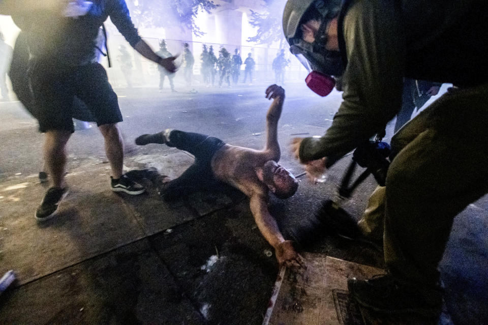 A protester lies on the ground as federal officers, seen in background, use chemical irritants to disperse Black Lives Matter demonstrators at the Mark O. Hatfield United States Courthouse on Friday, July 24, 2020, in Portland, Ore. Since federal officers arrived in downtown Portland in early July, violent protests have largely been limited to a two block radius from the courthouse. (AP Photo/Noah Berger)