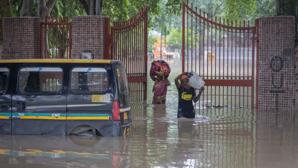 A couple carries their belongings as they leave a flooded cremation ground in New Delhi on July 13, 2023. - Adnan Abidi/Reuters