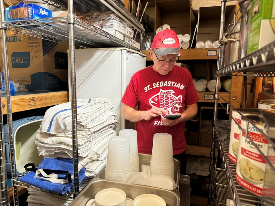 Mark Krier, who organizes the St. Sebastian Parish fish fry, reads text messages about volunteers who can't make it for their shifts while counting plastic lids in the cafeteria supply closet.