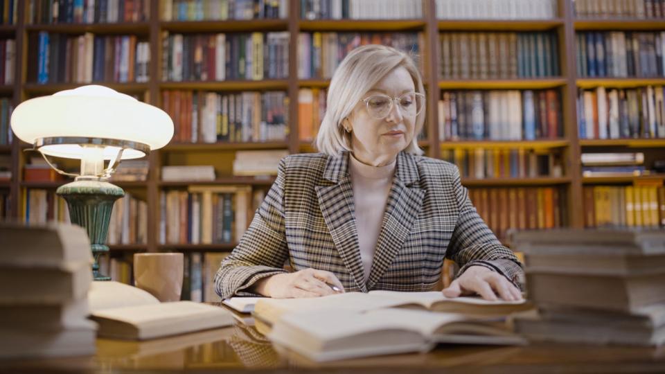 Woman in a library room reading through books on table in front of her.