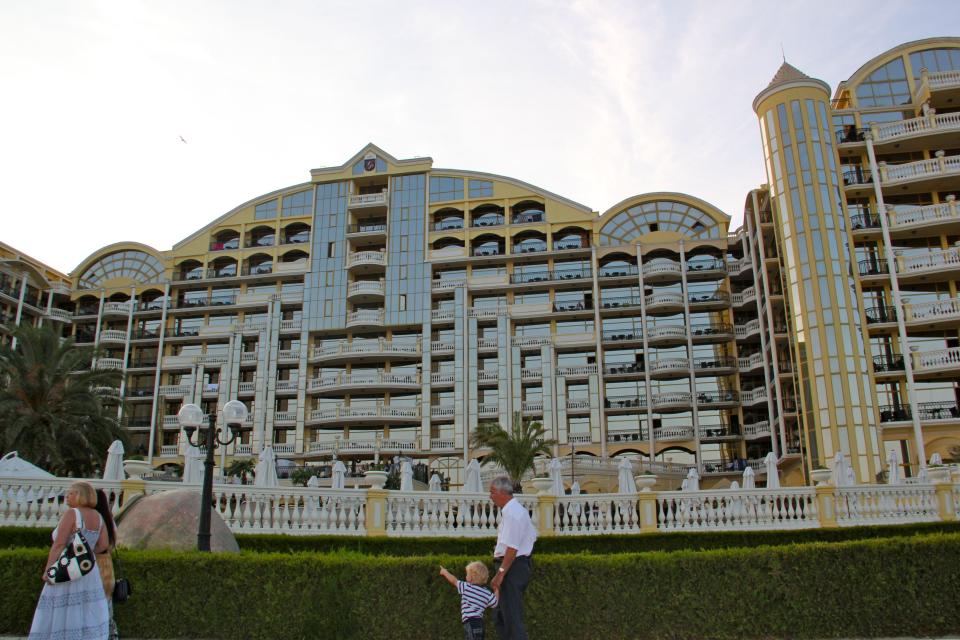 This Aug. 19, 2012 photo released by Mikhail Iliev shows visitors walking near the Victoria Palace hotel, one of several large resorts that line the Black Sea coast, in Sunny Beach Bulgaria. A visit to Bulgaria can alternately feel like taking like a step back in time and witnessing a society that has modernized at warp speed. Mules and Ferraris share the freeways. Near a store selling Prada and Versace clothes, old women peddle handmade crocheted doilies and embroidered tablecloths. Dilapidated Soviet-style apartment buildings teem with people, as does a sparkling new shopping mall. (AP Photo/Mikhail Iliev)