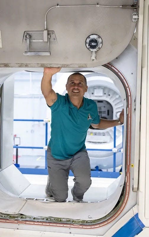 Astronaut Anil Menon kneels inside the entrance to a space craft