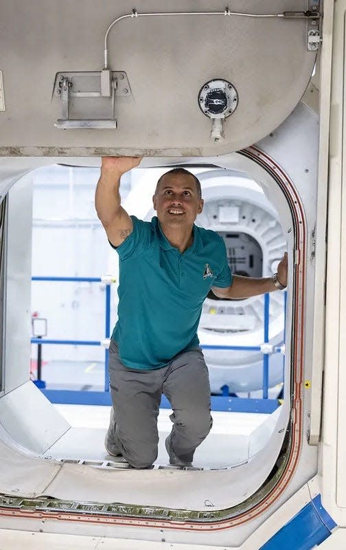 Astronaut Anil Menon is kneeling inside the entrance to a spaceship