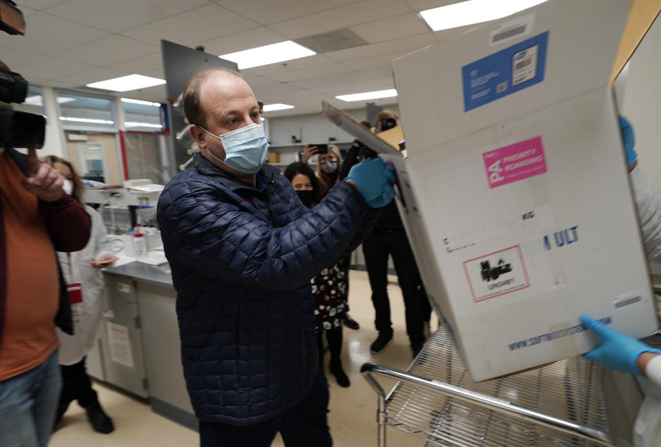 Colorado Governor Jared Polis helps put the state's first shipment of COVID-19 vaccine in a freezer with Patrick Belou, logisitics specialist at the laboratory for the Colorado Department of Public Health and Environment, early Monday, Dec. 14, 2020, in Denver.  (AP Photo/David Zalubowski)