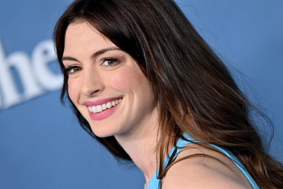 Anne Hathaway smiling in a close-up portrait, wearing a sleeveless top