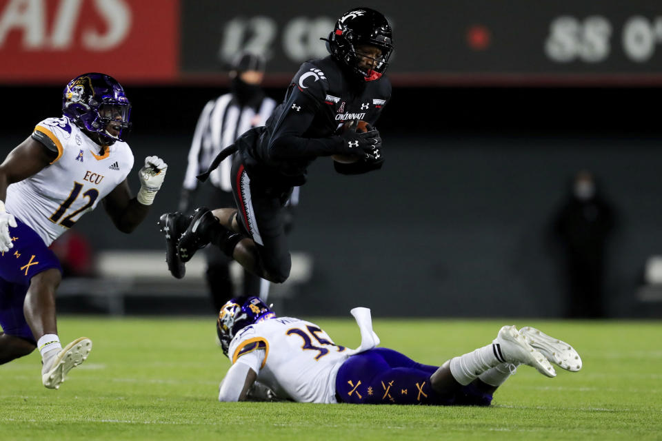 East Carolina linebacker Xavier Smith, left, defends as Cincinnati wide receiver Jordan Jones, middle, jumps over East Carolina defensive back Jireh Wilson during the first half of an NCAA college football game, Friday, Nov. 13, 2020, in Cincinnati. (AP Photo/Aaron Doster)