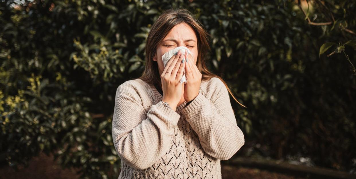 young woman suffering spring allergy and blowing nose with a tissue in the nature