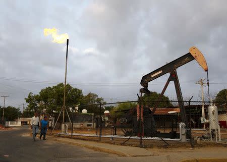 Two people walk past an oil pump in Lagunillas, Ciudad Ojeda, in the state of Zulia, Venezuela, March 18, 2015. REUTERS/Isaac Urrutia