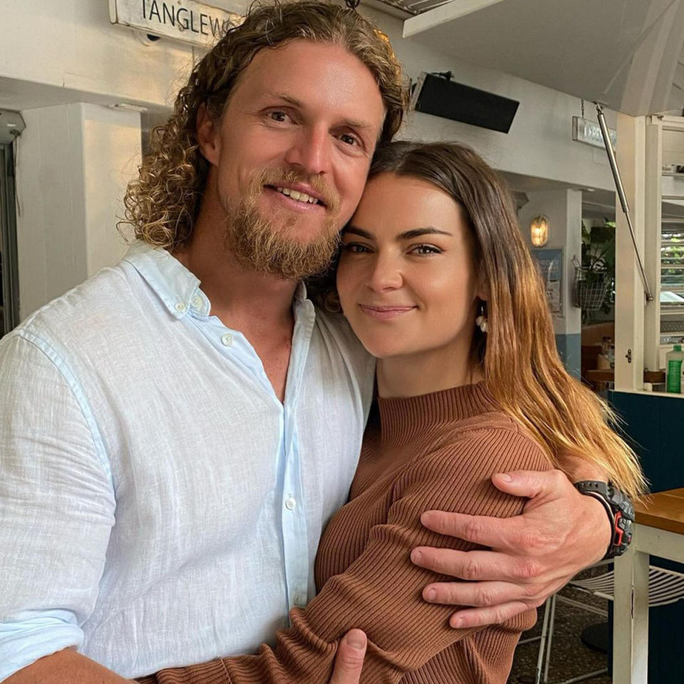 Nick Cummins in a light blue shirt and Alexandra George in a brown top are smiling for the camera while hugging