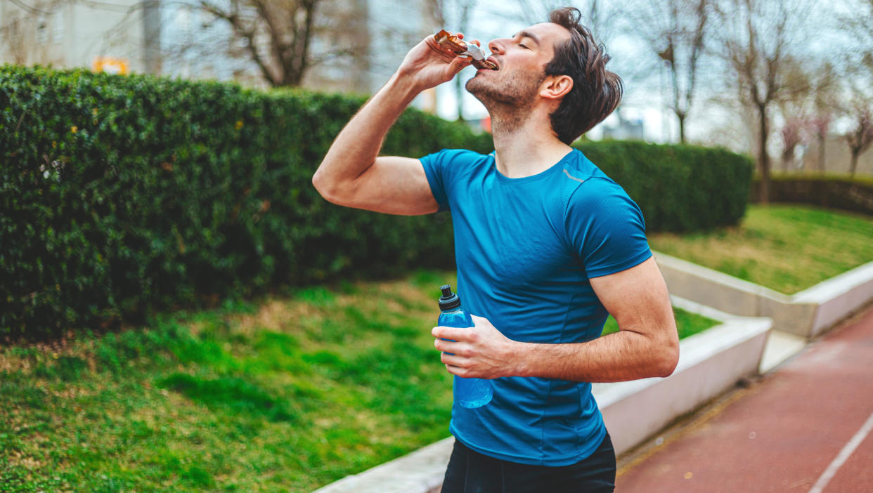  A male runner biting into a snack bar . 
