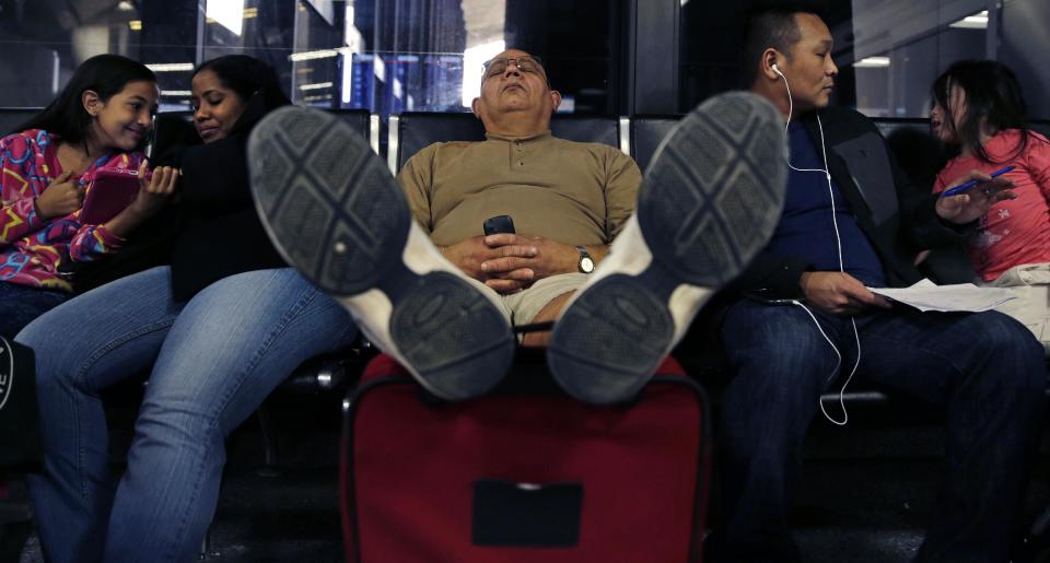 Eli Lopez, of New Bedford, Mass., rests his feet on his luggage while taking a nap after his flight to Puerto Rico was canceled, at Logan International Airport, Monday, Jan. 6, 2014, in Boston. Heavy rains in the East, and sub-zero temperatures in the Midwest, created havoc for airlines and travel plans. Lopez said he was rebooked on a flight Thursday. (AP Photo/Charles Krupa)