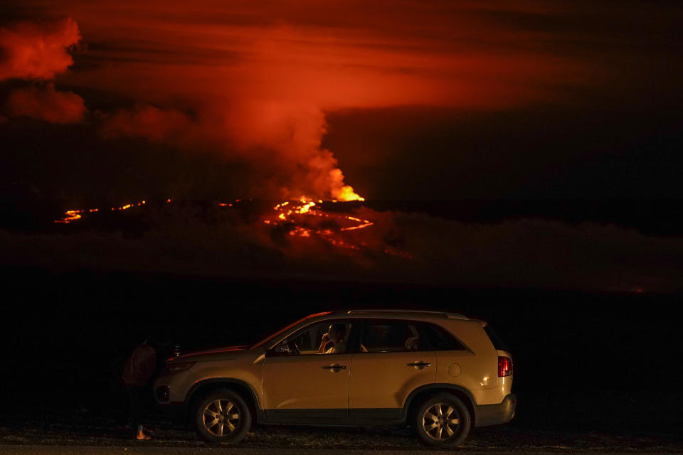 A man talks on a phone in his car alongside Saddle Road as the Mauna Loa volcano erupts Wednesday, Nov. 30, 2022, near Hilo, Hawaii. Hundreds of people in their cars lined Saddle Road, which connects the east and west sides of the island, as lava flowed down the side of Mauna Loa and could be seen fountaining into the air on Wednesday. (AP Photo/Gregory Bull)