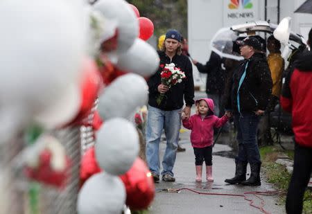 Chris Green (L) and Angela Green (3rd L), both graduates of Marysville-Pilchuck High School, walk with their daughter Dorothy, 2, as they take flowers to the makeshift memorial outside the school in Marysville, Washington October 25, 2014. Relatives of a Washington state teen accused of a high school shooting rampage said on Saturday that they were living in a "nightmare" and struggling to understand why the boy targeted his two cousins and several friends before killing himself. One girl was killed and four other freshman students were severely wounded in Friday's morning rampage inside the cafeteria at Marysville-Pilchuck High School, north of Seattle. REUTERS/Jason Redmond (UNITED STATES - Tags: CRIME LAW SOCIETY EDUCATION)