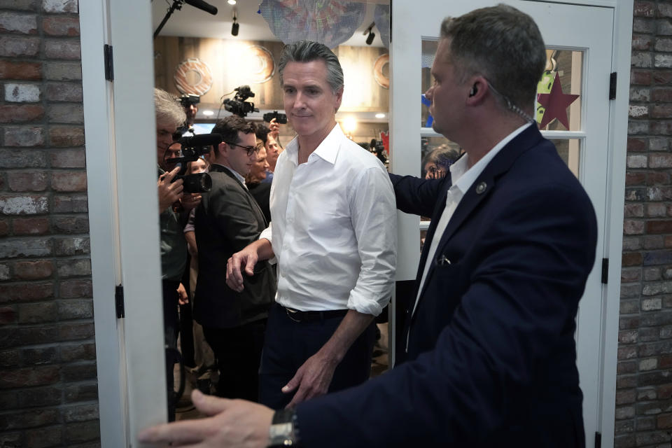 California Gov. Gavin Newsom, center, is escorted by a security official, right, as he steps out of a donut shop, Monday, July 8, 2024, in Hooksett, N.H. (AP Photo/Steven Senne)