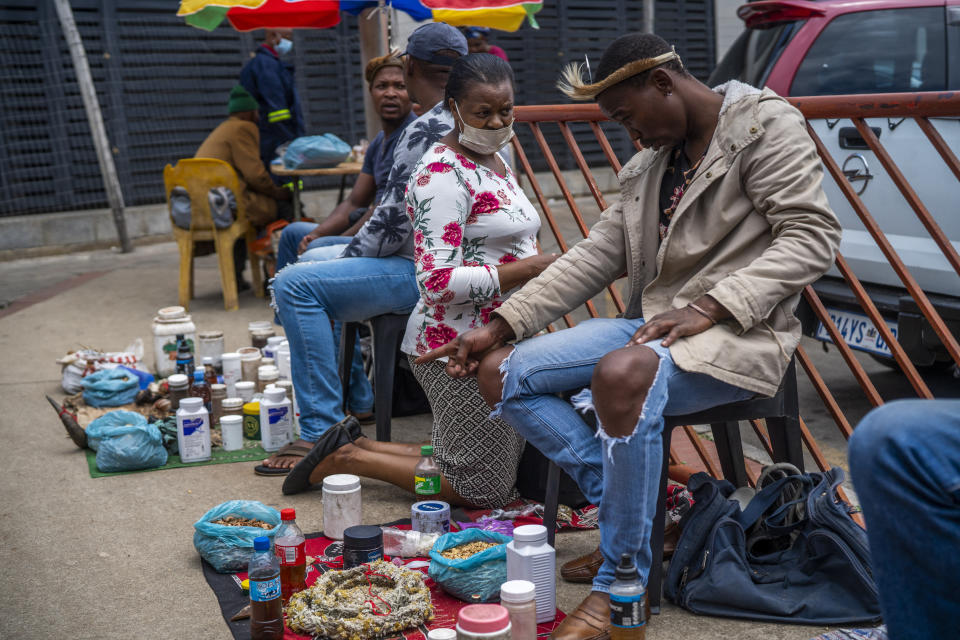 A woman consults a traditional doctor near the Baragwanath taxi rank in Soweto, South Africa, Thursday Dec. 2, 2021. Fearing vaccines, some turn to traditional doctors for COVID-19 remedies. South Africa launched an accelerated vaccination campaign to combat a dramatic rise in confirmed cases of COVID-19 a week after the omicron variant was detected in the country. (AP Photo/Jerome Delay)