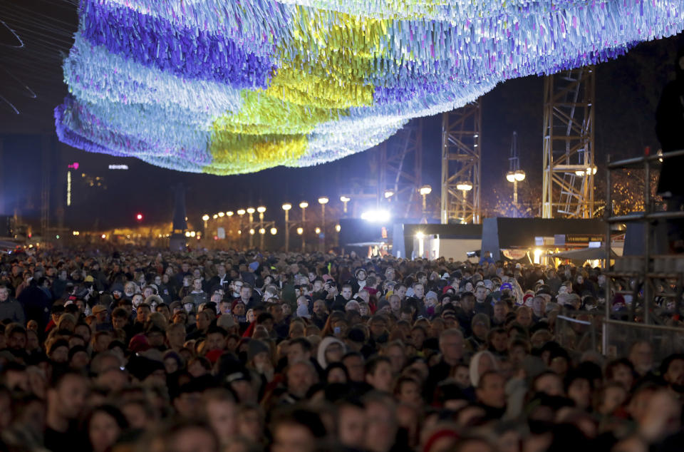 Visitors stay underneath the skynet artwork 'Visions In Motion' in front of the Brandenburg Gate as they attend stage presentations to celebrate the 30th anniversary of the fall of the Berlin Wall in Berlin, Germany, Saturday, Nov. 9, 2019. (AP Photo/Michael Sohn)