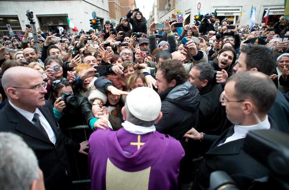 In this photo provided by the Vatican paper L'Osservatore Romano, Pope Francis greets faithful from a side gate of the Vatican, Sunday, March 17, 2013. Pope Francis began his first Sunday as pontiff by making an impromptu appearance to the public from a side gate of the Vatican, startling passersby and prompting cheers, then kept up his simple, spontaneous style by delivering a brief, off-the-cuff homily at the Vatican's tiny parish church. Dressed only in white cassock, Francis waved to the crowd in the street outside St. Anna's Gate and before entering the church, which serves Vatican City State's hundreds of residents, he shook hands of the parishioners and kissed babies. (AP Photo/L'Osservatore Romano)