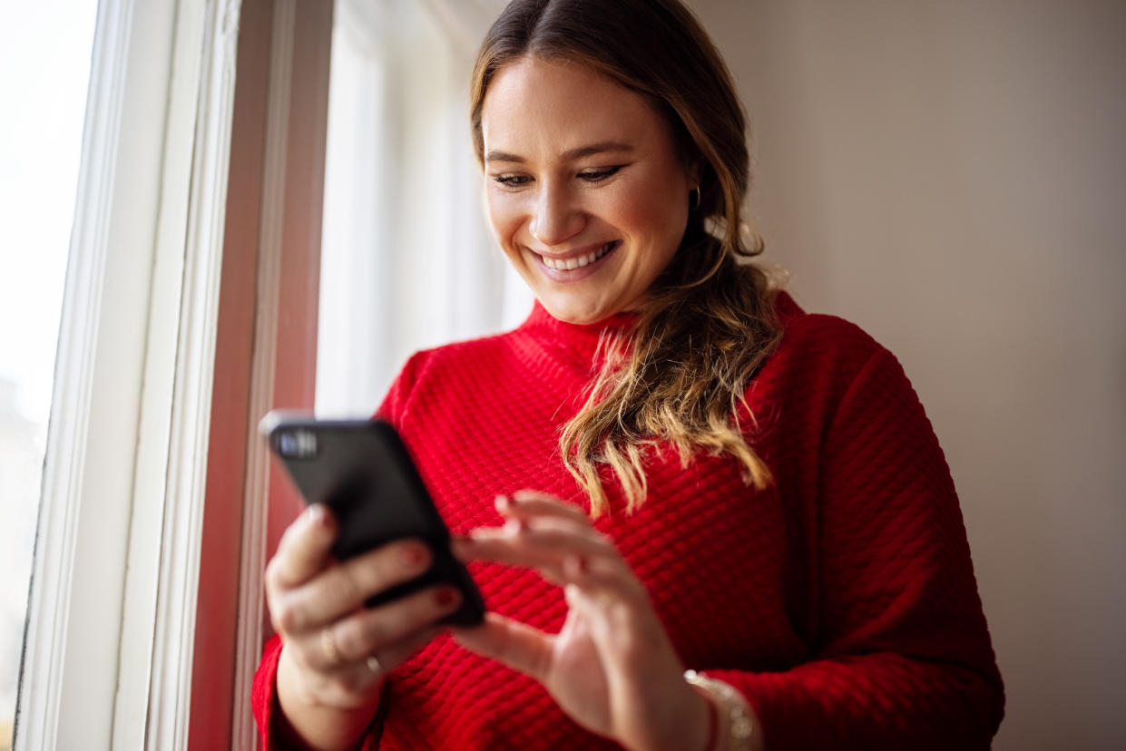 Young woman texting on her smartphone and smiling. Female reading text messaging on her mobile phone.