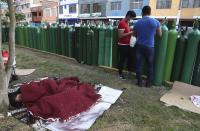 People sleep next to their empty oxygen tanks as many wait for the refill shop to open in Callao, Peru, Monday, Jan. 25, 2021, amid the COVID-19 pandemic. Some said they arrived to get in line on Sunday after the store closed to be first on Monday, while others missed out on Sunday's allotments of refills, approximately 80 tanks, and stayed a second day to wait. (AP Photo/Martin Mejia)