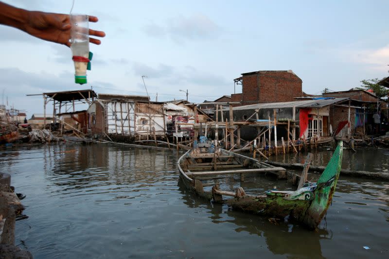 A damaged wooden boat is pictured as a man fishes at Tambaklorok village, which has been affected by rising sea level and land subsidence, in Semarang