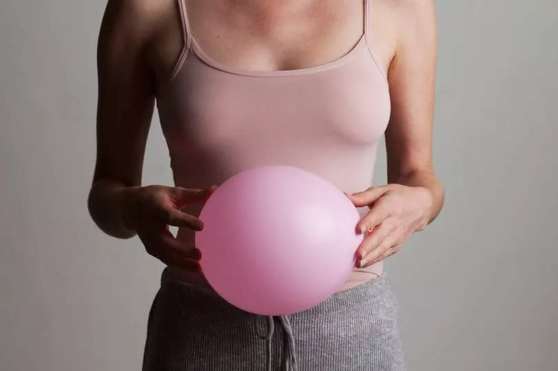 Young woman holding inflated pink balloon in front of her stomach