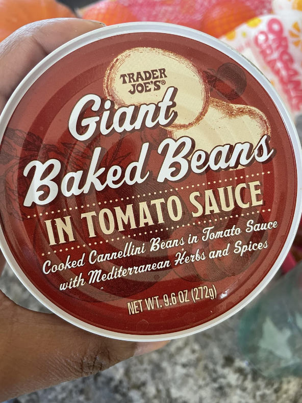 Hand holding a can of Trader Joe's Giant Baked Beans in tomato sauce with Mediterranean herbs and spices