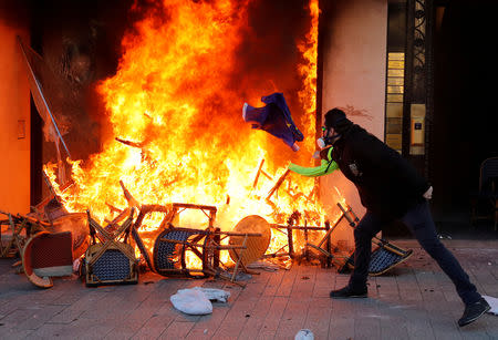 A protester throws an EU flag into the fire of a burning shop during a demonstration by the "yellow vests" movement in Paris, France, March 16, 2019. REUTERS/Philippe Wojazer