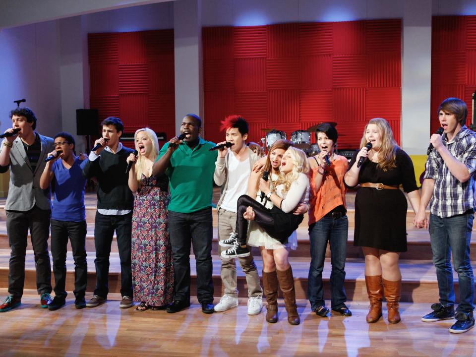 The cast of "The Glee Project" season two singing in a straight line with microphones.