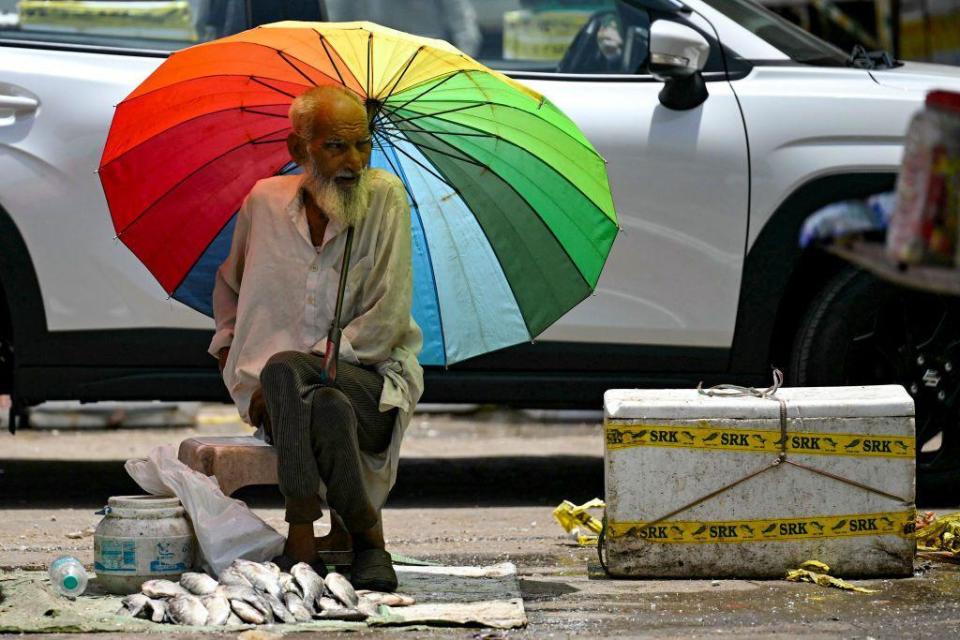 A fish vendor waiting for customers takes shade under an umbrella on a hot summer afternoon in New Delhi on May 29, 2024, amid ongoing heatwave.