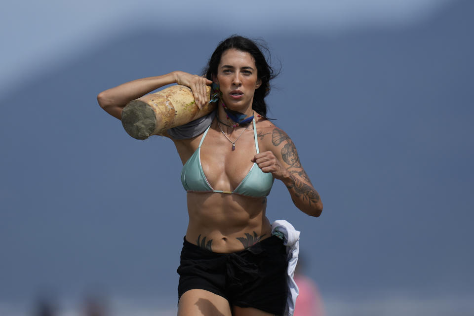 Una deportista compite en una carrera de relevos, cargando troncos, en la playa de Peruibe, como parte de los Juegos Indígenas, cerca de la comunidad Tapirema, en Peruibe, Brasil, el 23 de abril de 2023 (AP Foto/Andre Penner)