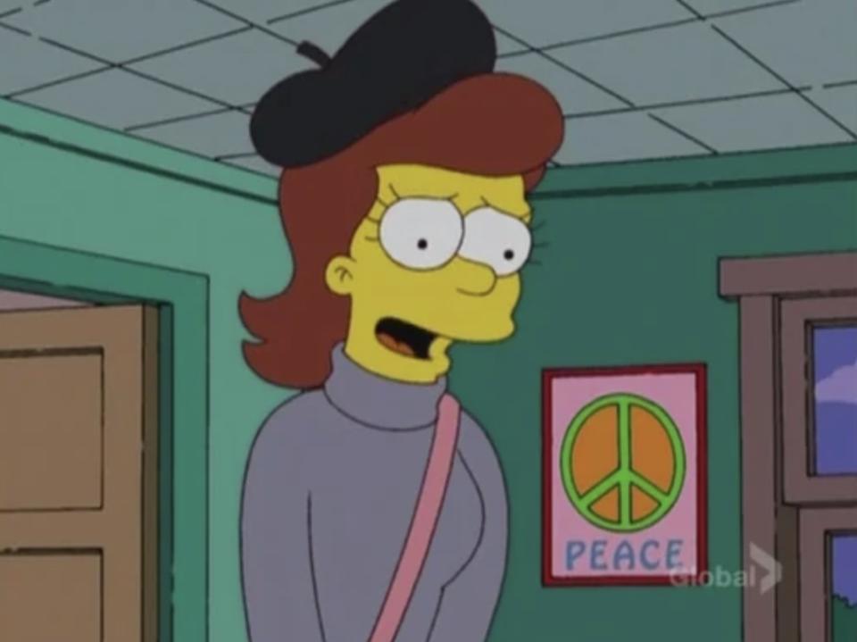 A young woman wearing a beret stands in a room, there's a 'peace' poster hanging on the wall behind her