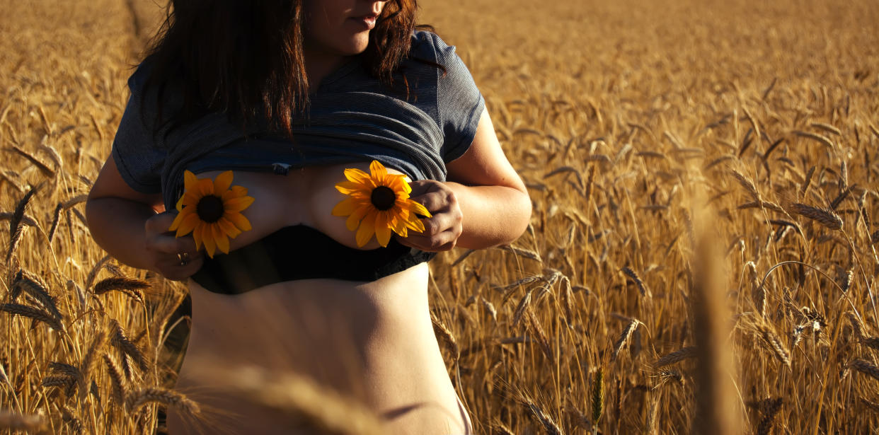 Close-Up Of Woman Covering Breast With Flower While Standing On Field