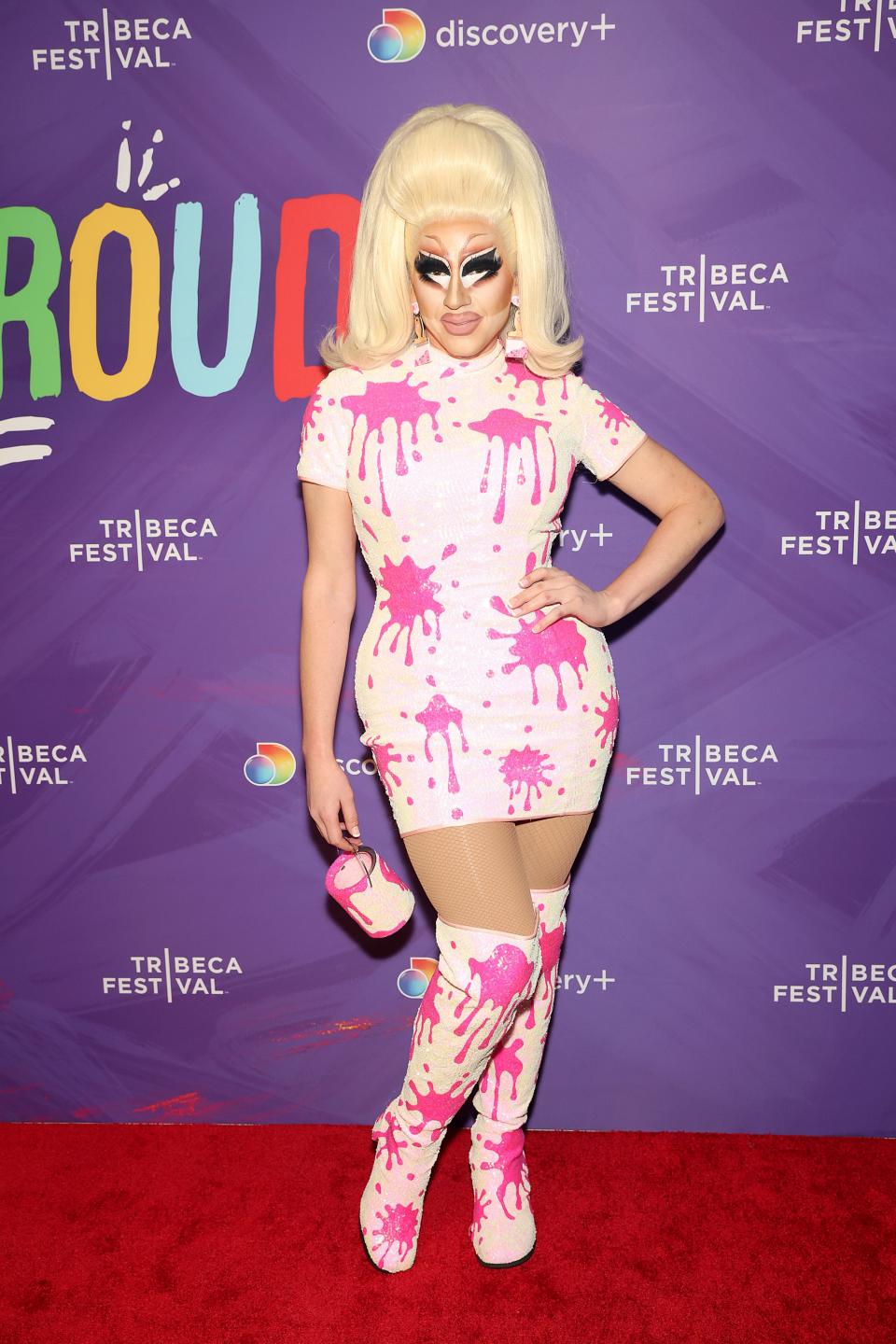 Trixie Mattel poses in a red carpet on a pink splatter mini dress and matching boots