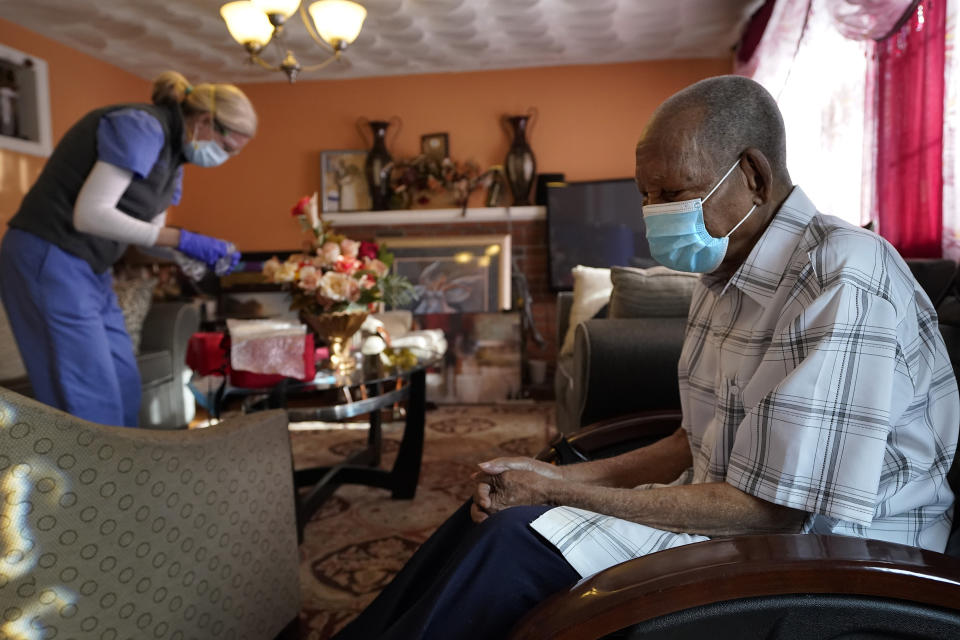 Edouard Joseph, 91, right, clasps his hands as geriatrician Megan Young, left, prepares to give him a COVID-19 vaccination, Thursday, Feb. 11, 2021, at his home in the Mattapan neighborhood of Boston. Millions of U.S. residents will need COVID-19 vaccines brought to them because they rarely or never leave home. Doctors and nurses who specialize in home care are leading this push and starting to get help from state and local governments around the country. (AP Photo/Steven Senne)